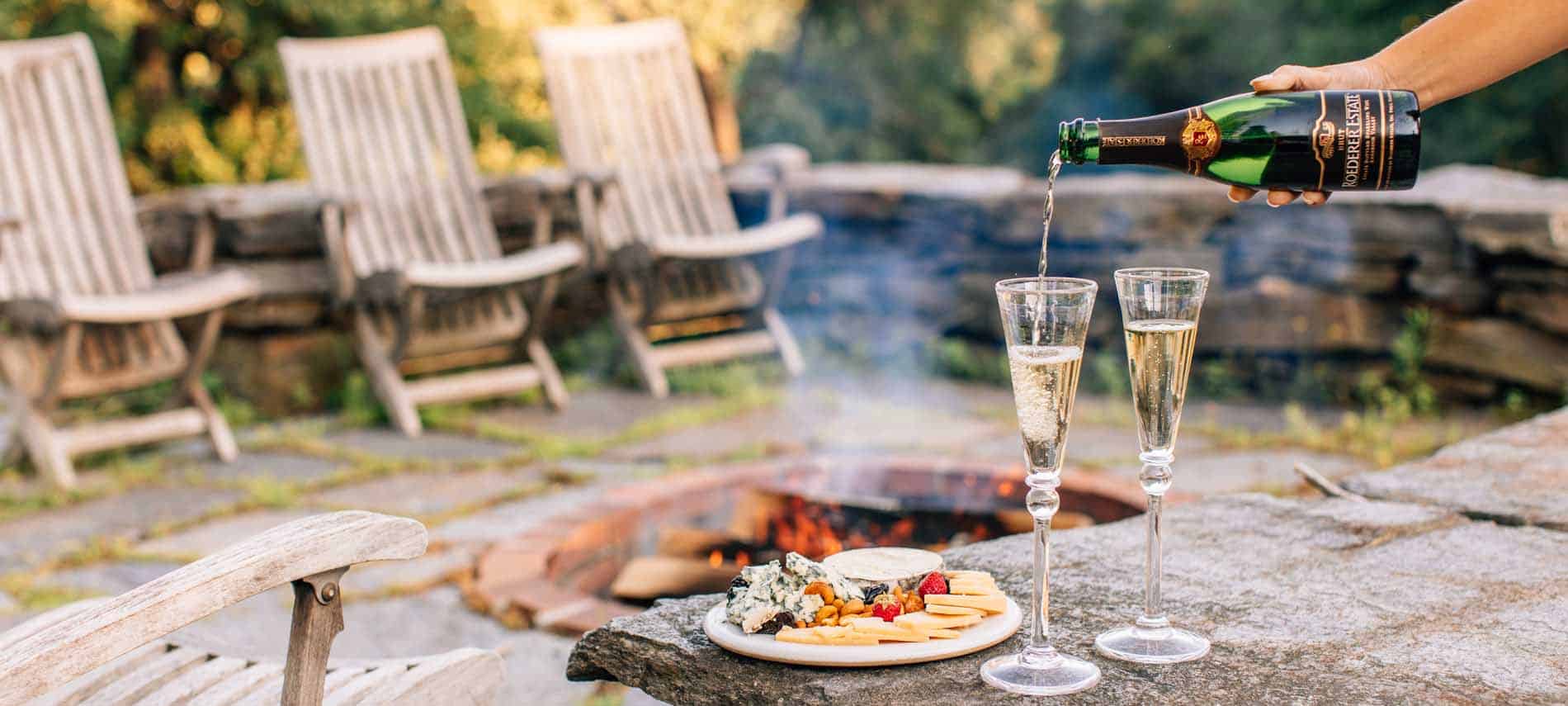 hand pouring champagne by stone firepit