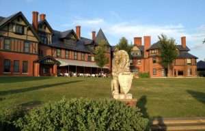 palacial brick building on a green lawn fronted by a lion statue