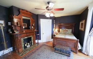 blue bedroom with large wood bed and ornate wood mantle fireplace