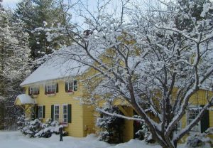 yellow house with a snow covered roof and lawn