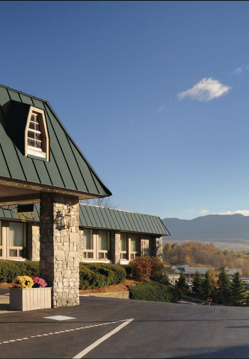 Front entry of hotel on top of hill in summer with view of mountains.