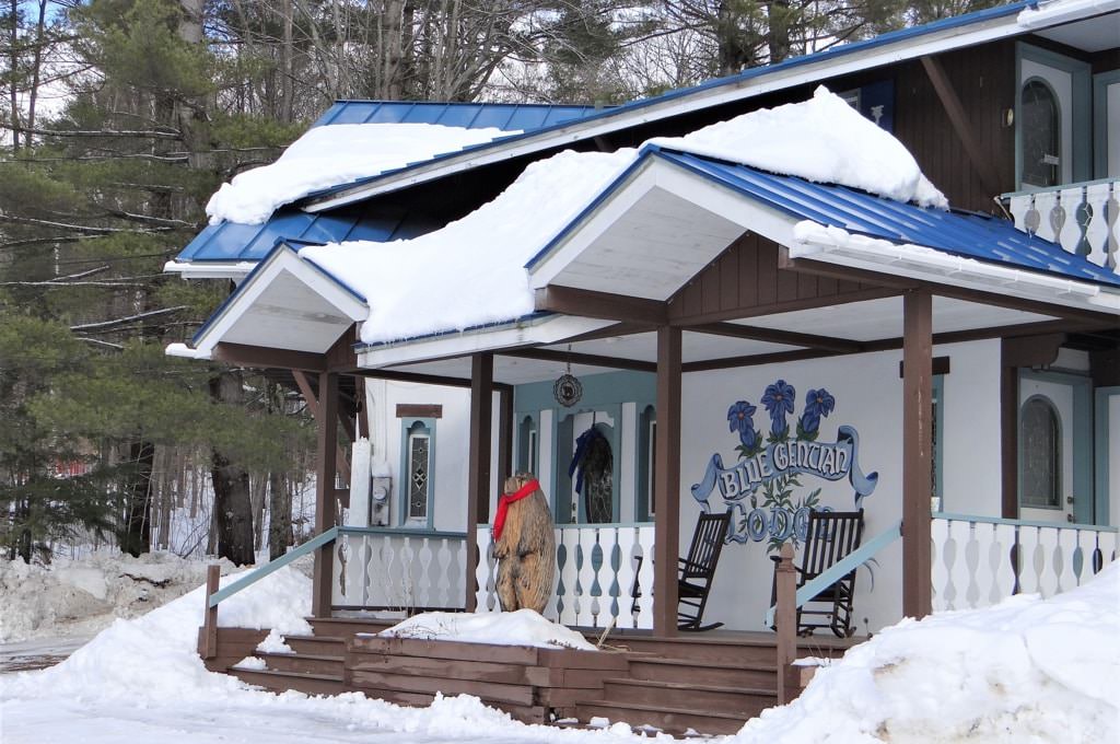 Front view of home painted white and brown with blue metal roof surrounded by snow