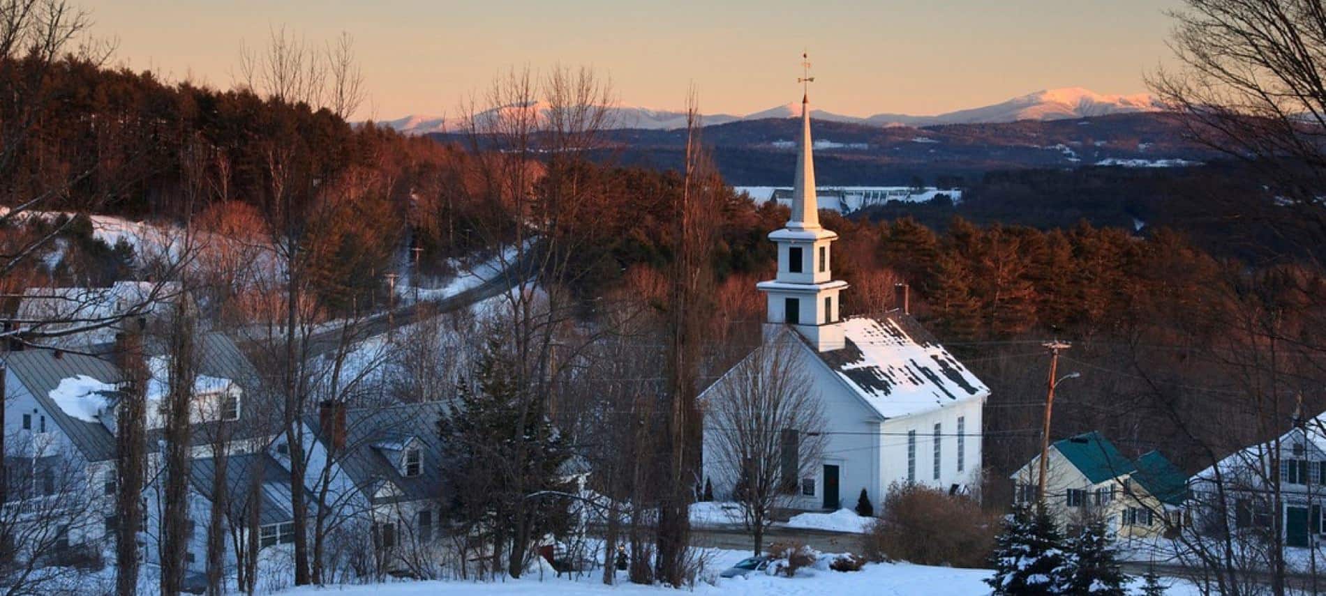 Aerial view of Vermont town in winter with hills, curvy roads, snow-topped buildings and white church with steeple