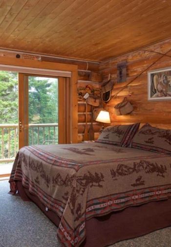Rustic guest room with wood walls and ceiling, sliding doors to balcony and bed