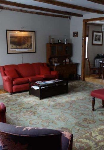 Common sitting room with wood floors, large rug, exposed beams and upholstered furniture